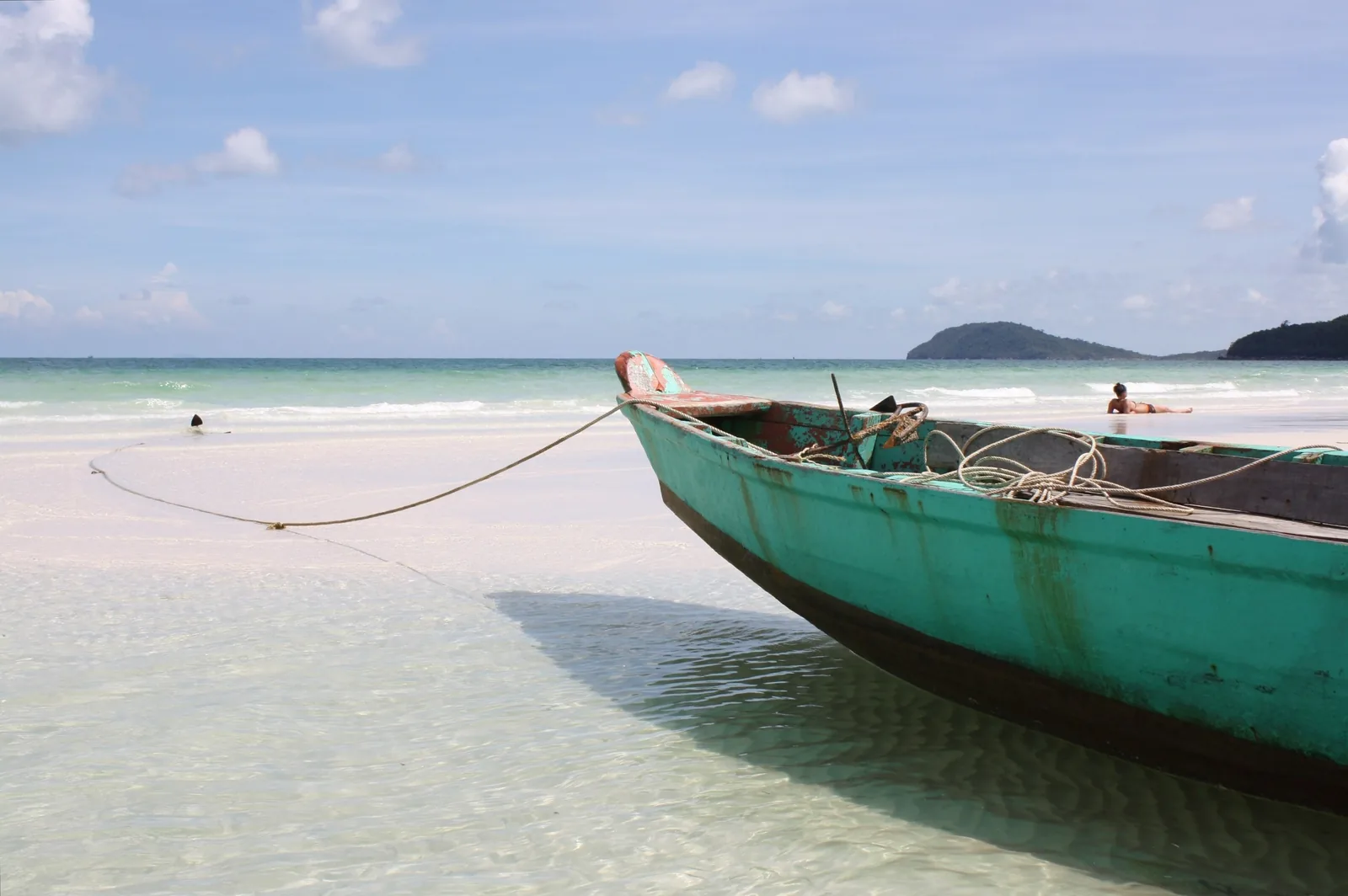A green wooden boat rests in shallow turquoise water off a white sand beach in Phu Quoc.